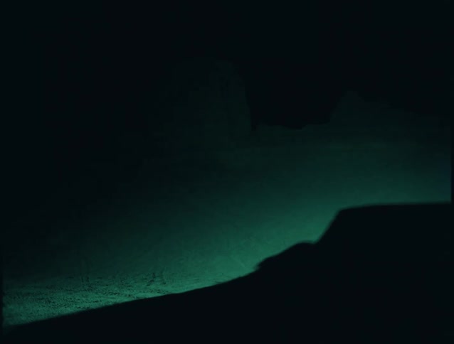 A silhouetted car with a roof box glides through the dark its shape outlined by a teal glow on a wall