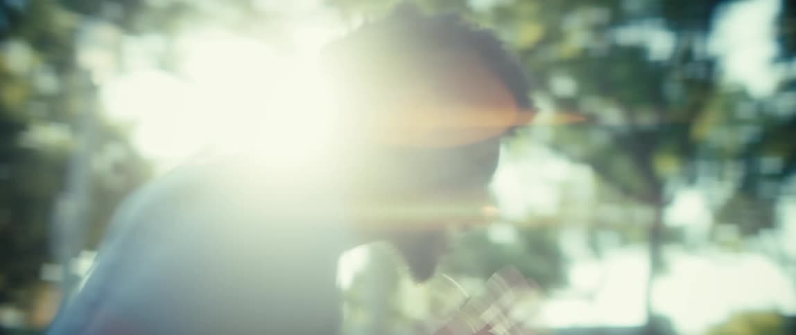 An athlete runs away from the camera through a sunlit park