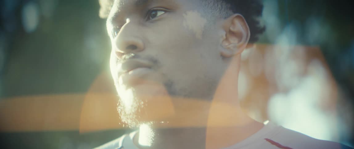 A black mans hands are clasped together as he stands in bright sunlight
