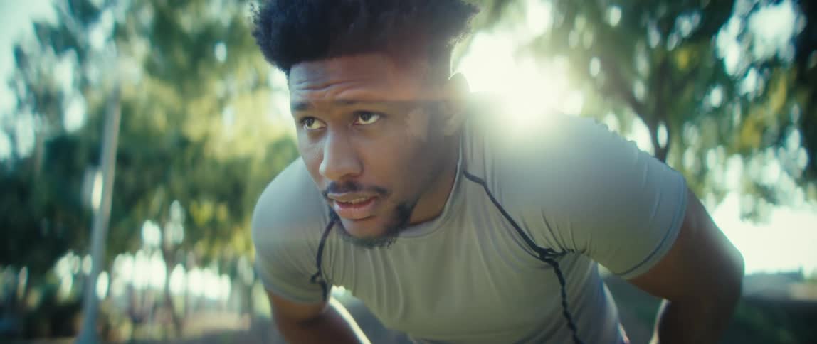A young black man stands under the bright sun visibly tired after completing an outdoor workout his posture relaxed as he catches his breath in the open air