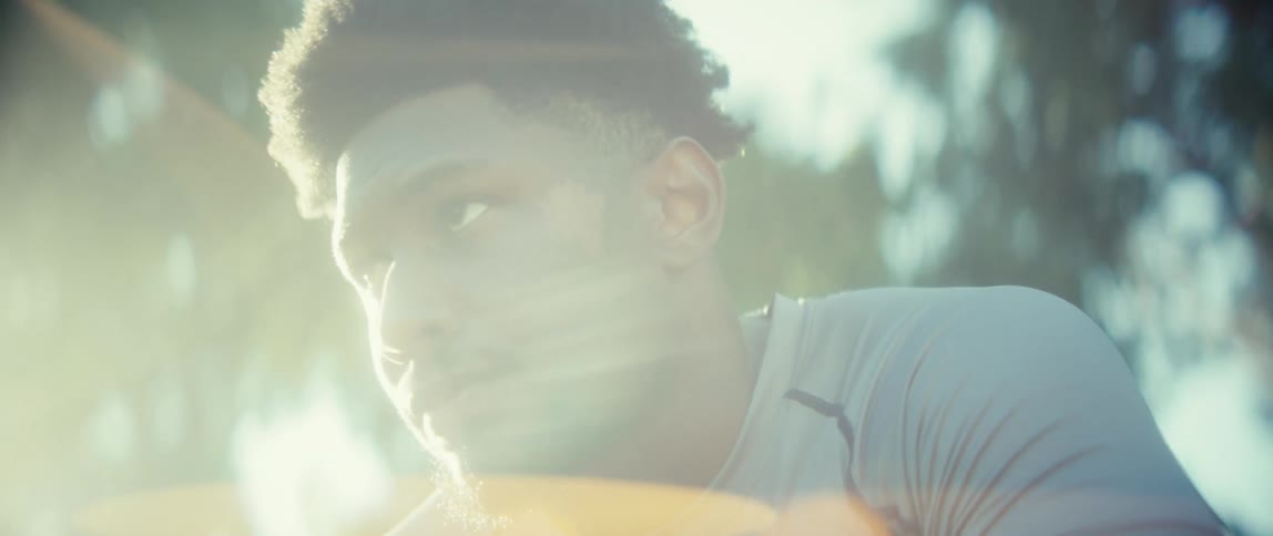 A close view shows a sweaty man with an afrostyle haircut and beard taking a deep breath after exercise outdoors with bright sunlight creating lens flares