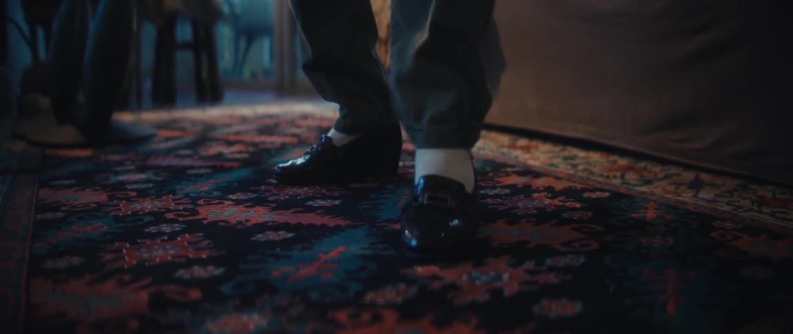 A persons feet in loafers tapping and dancing on a patterned rug