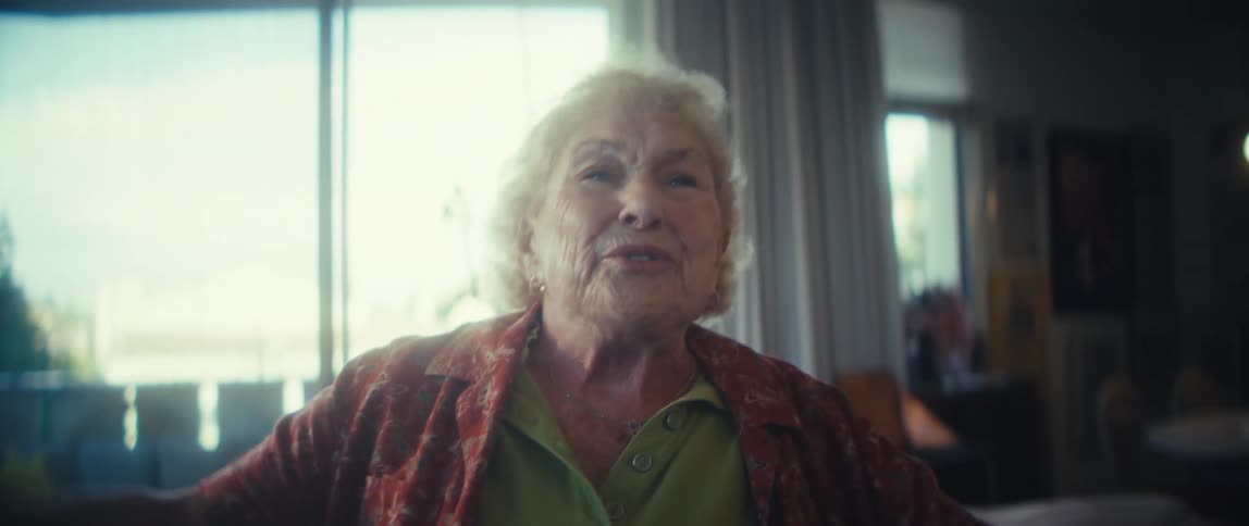 An elderly woman jumps up and joyfully dances in her living room