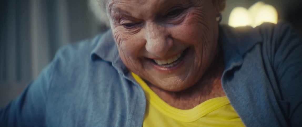 An elderly woman smiles lovingly as she pets her fluffy dog