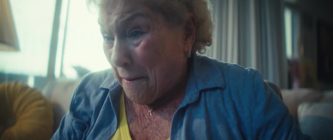 An elderly woman sits on a couch in her living room at midday excited as she watches a game