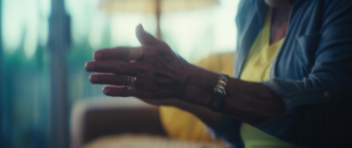 An elderly female sitting in a living room is excited and clapping her hands and clenching her fists