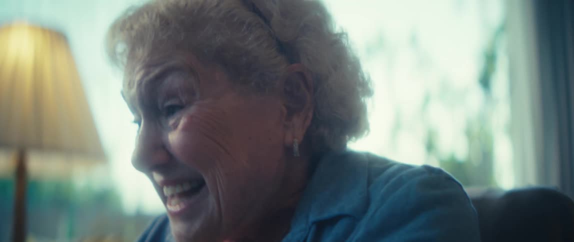 An elderly woman sits in a cozy living room at noon her face bright with excitement as sunlight fills the room