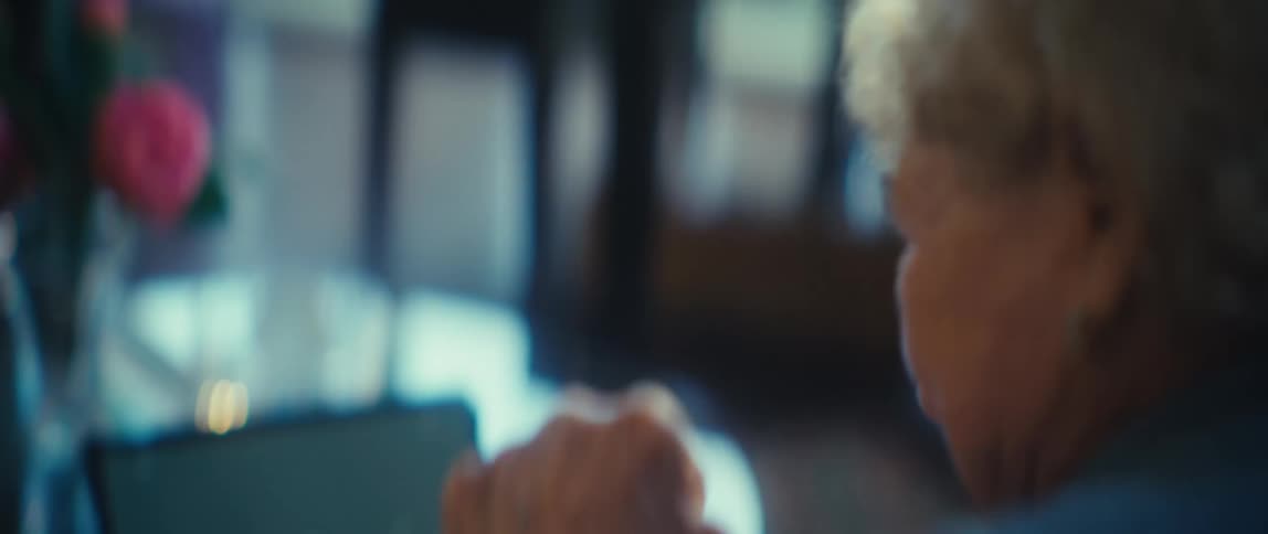 Elderly woman watching a tablet celebrates while sitting at home