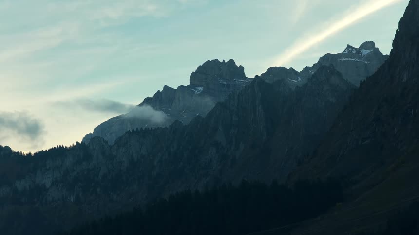 Rocky mountains covered with vegetation and snow under a light blue sky