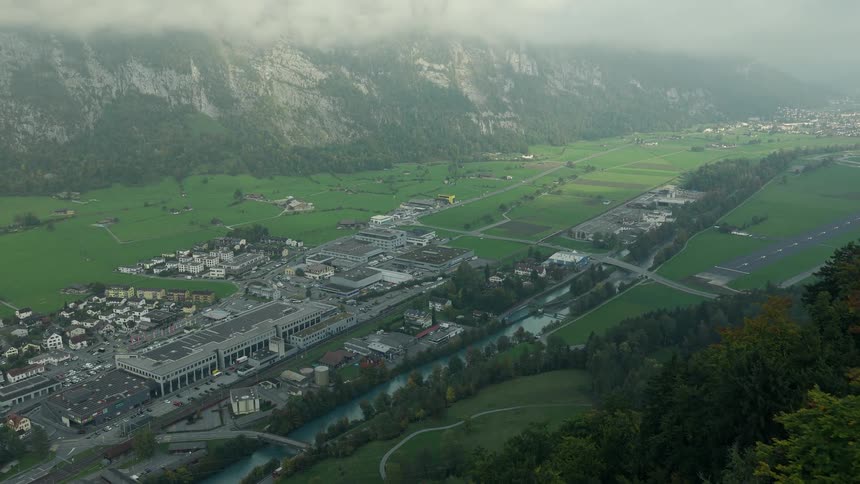 Reveal of a typical Swiss town in a long misty valley at the base of steep mountains with a train passing by
