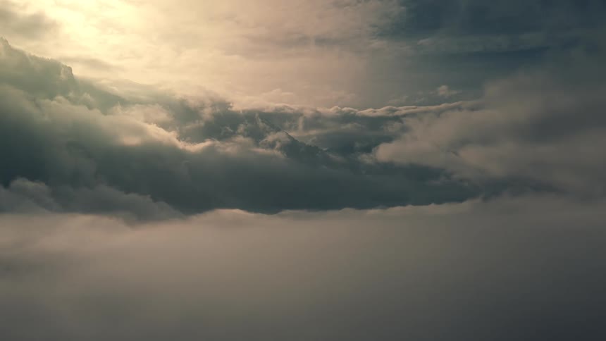 A dense formation of moving gray and white clouds from above with a strong light source at the top left casting a bright glow and creating strong contrast between the layers of cloud cover