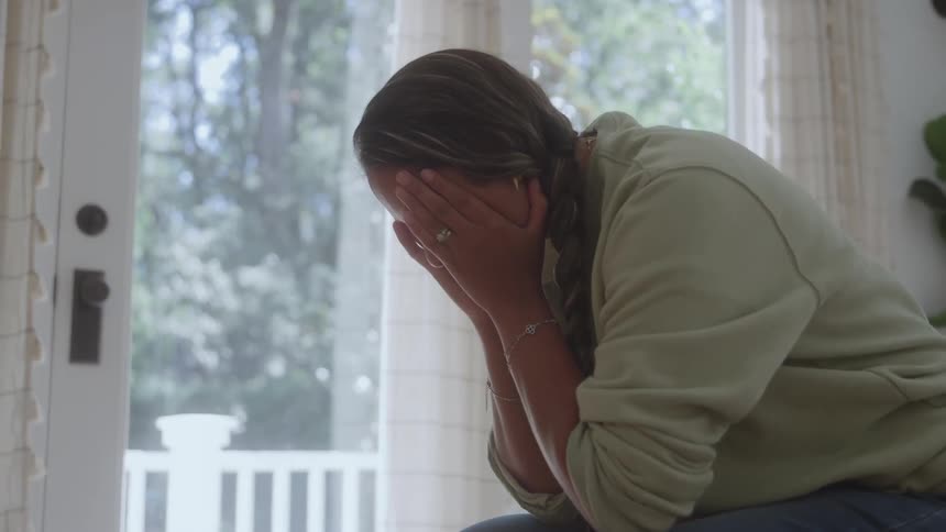 The woman sits with her face in her hands