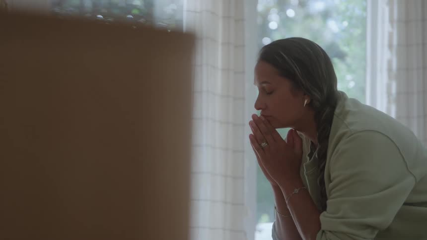 A young woman praying while sitting in a room during daytime