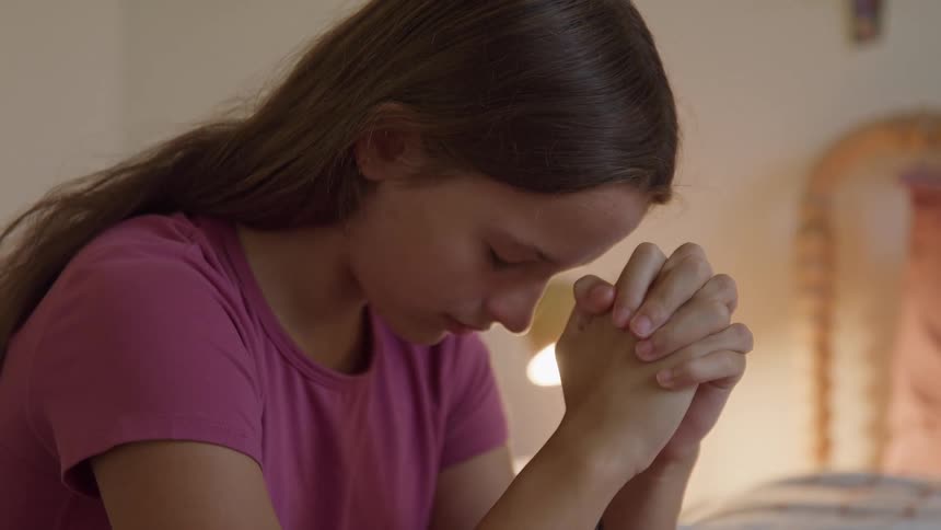 The girl is praying in her bedroom