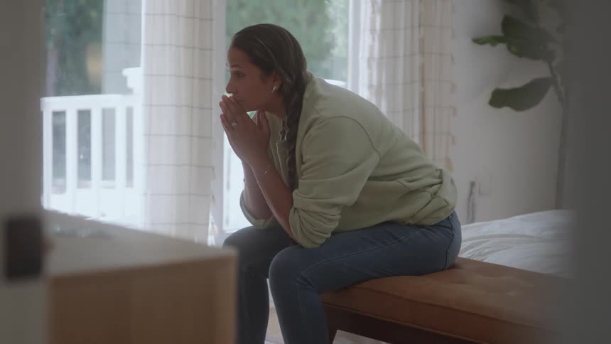 A young woman thinking while sitting on a bed in a bedroom during daytime