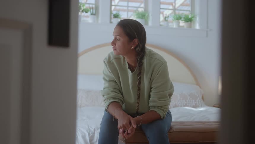 A young woman thinking while sitting on a bed in a bedroom during daytime