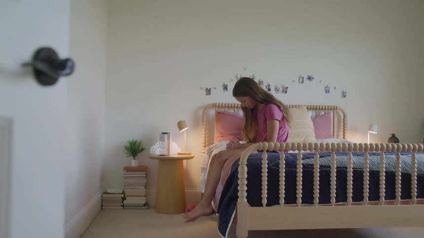 Girl sits on her bed with her head bowed as she prays