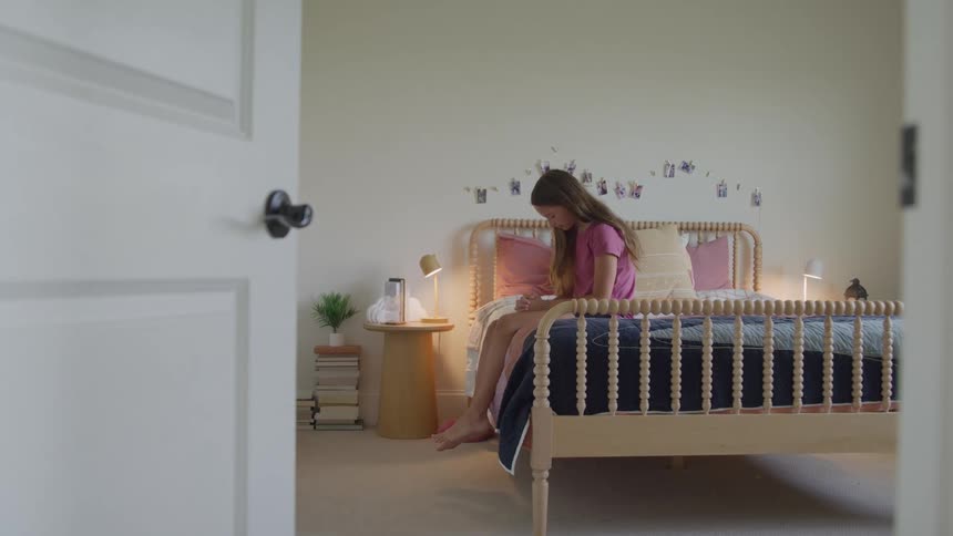 A female teenager praying while sitting on her bed in her bedroom during daytime