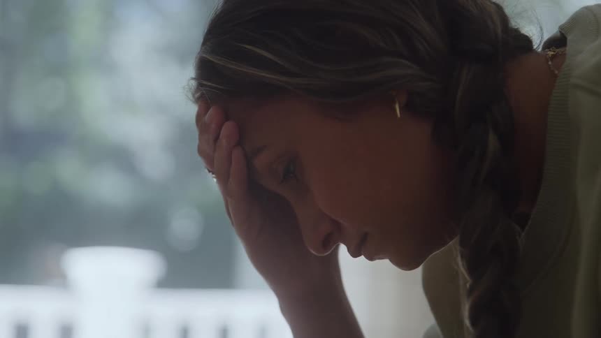 A female appearing stressed and sad has her hand pressed on her head looking down