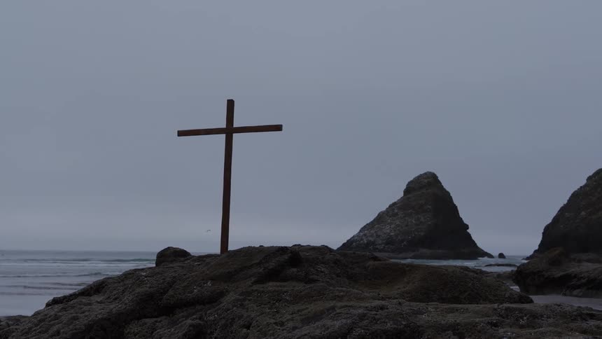 Wooden cross standing on rocks by the sea on a cloudy day