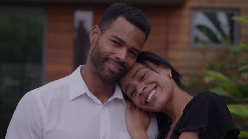 Smiling couple embracing in front of a wooden house