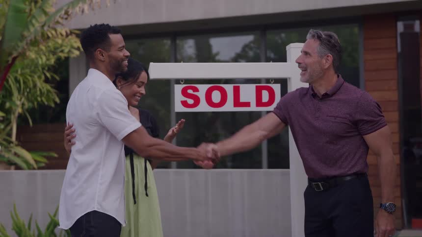 The video clip features a diverse couple embracing while a real estate agent smiles and shakes the hand of the man presumably celebrating a home purchase a sold sign is clearly visible in the window of the house behind the three individuals