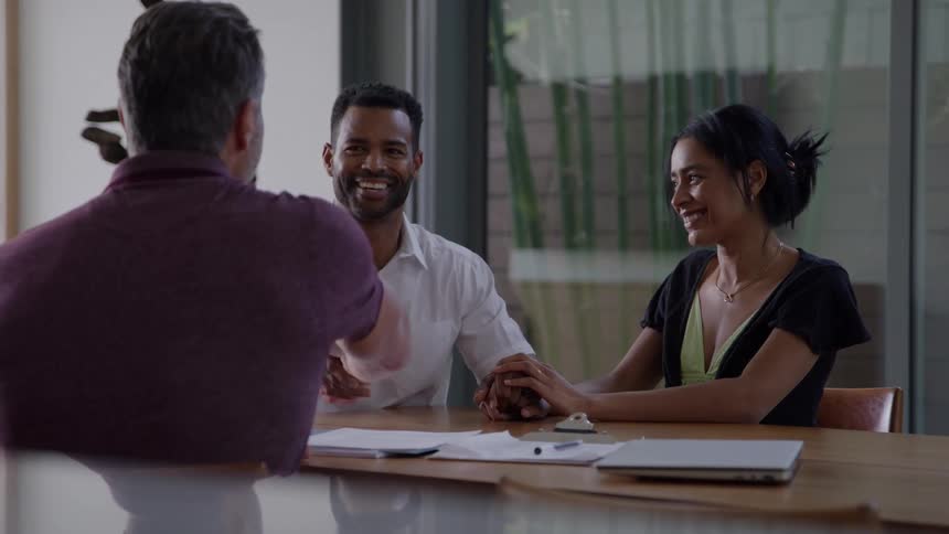 Smiling couple shaking hands with a man during a meeting at a wooden table