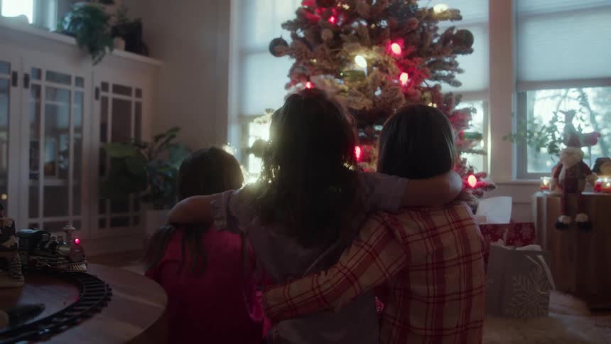 The video clip shows an unfocused shot of a christmas tree decorated with colorful lights situated near a large window creating a festive atmosphere a bright lens flare dominates the center of the frame obscuring much of the details and lendin