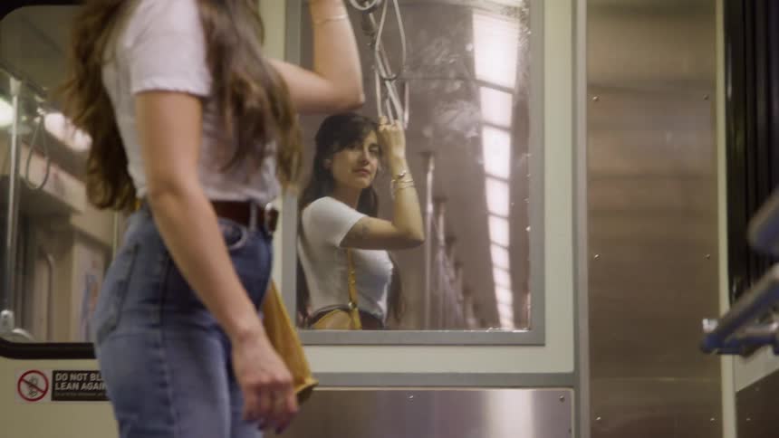 A young woman holds onto a grab rail while standing in a subway car