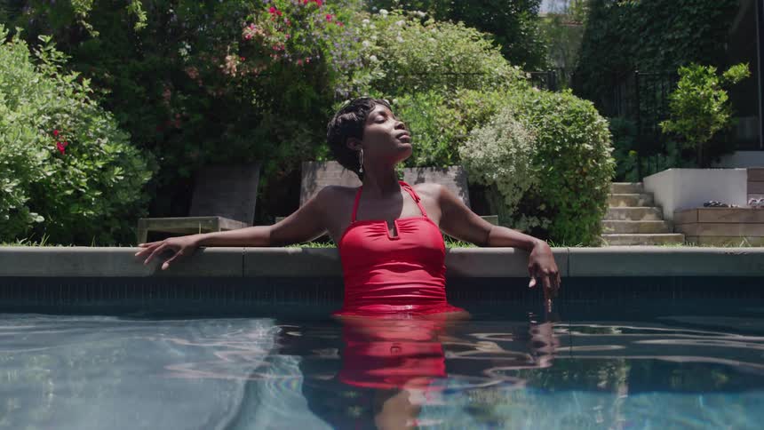 Woman in a red swimsuit relaxing in the pool under the sun in a garden