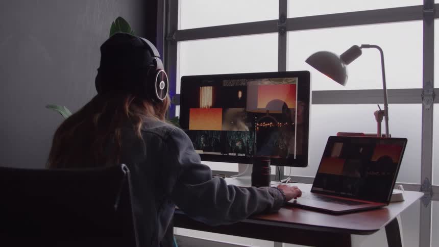 Person wearing headphones working on video editing in front of two monitors