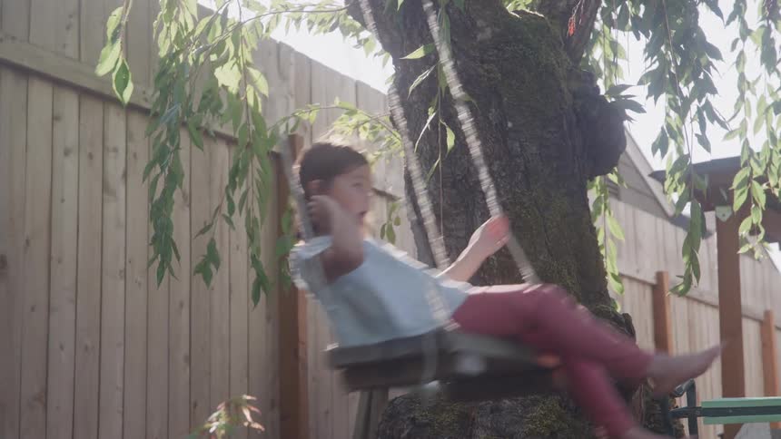 Girl playing on a swing tied to a tree under sunlight