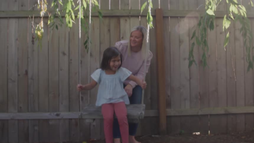 A mother smiles while pushing her daughter on an outdoor tree swing