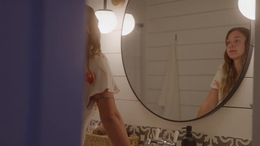 Woman staring at her reflection in a brightly lit bathroom mirror