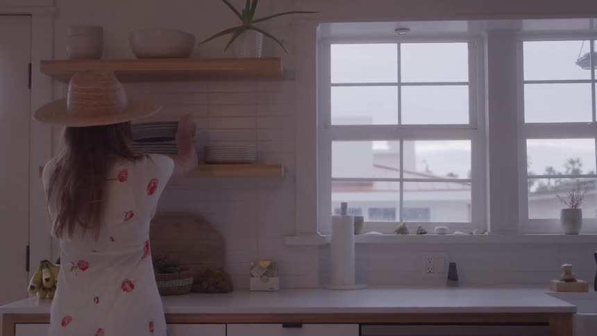 The woman puts dishes on the shelf in the kitchen