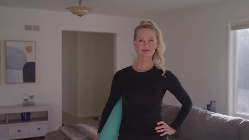 Woman in sportswear holding a yoga mat in a bright living room