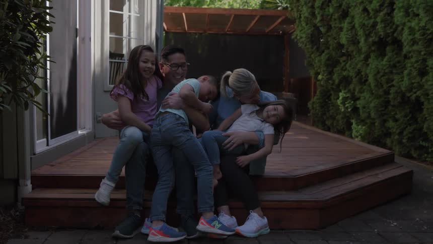 Parents hold their children on their laps while sitting outside on their deck