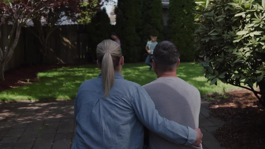 A man and a woman are sitting looking at some children playing on a lawn