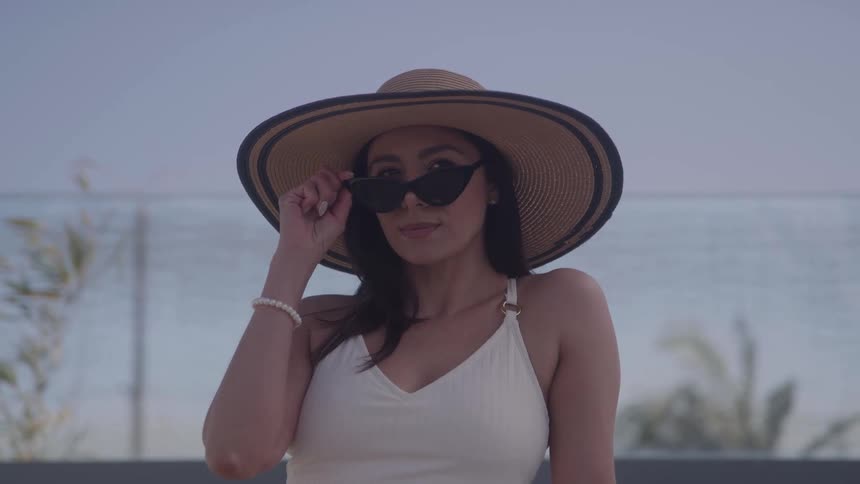 Woman wearing a widebrimmed hat adjusting her sunglasses under the sunlight