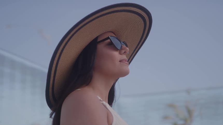 A stylish woman wearing a wide brimmed straw hat and sunglasses looks up at the sky