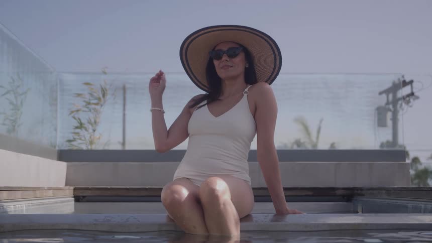 Woman sitting by the pool wearing a widebrimmed hat and sunglasses on a sunny day