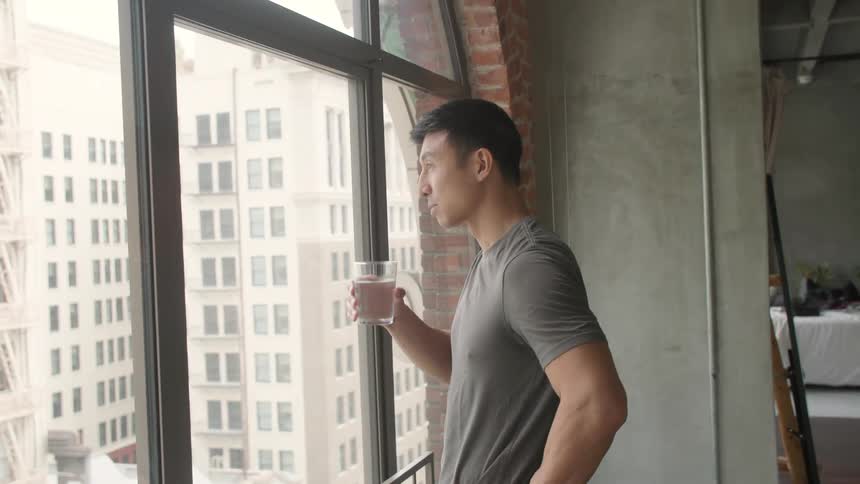 Man looking out the window at the city while drinking a glass of water
