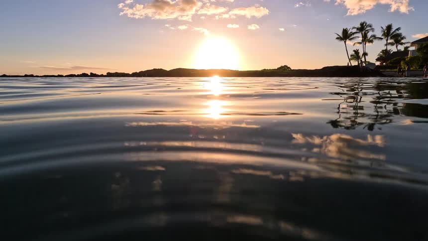The surface of the water with small ripples and the sun shining on the horizon