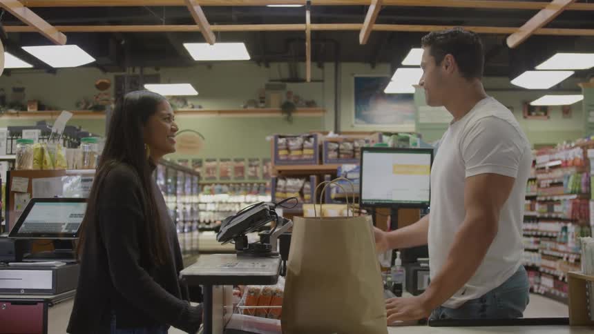 Customer and cashier smiling while talking at the grocery checkout