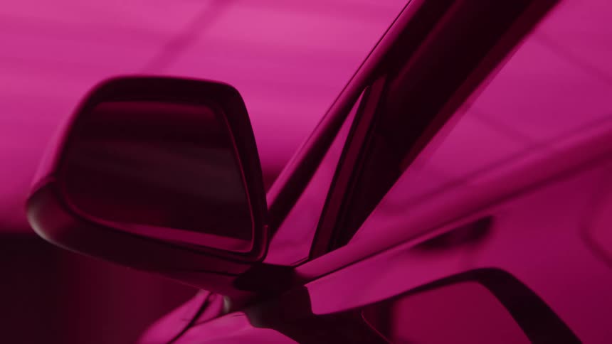 The video is a closeup shot of a cars sideview mirror and part of the door frame against a solid brightly colored backgroundthe entire frame is bathed in an intense artificial magenta or hot pink light giving the scene a vibrant high