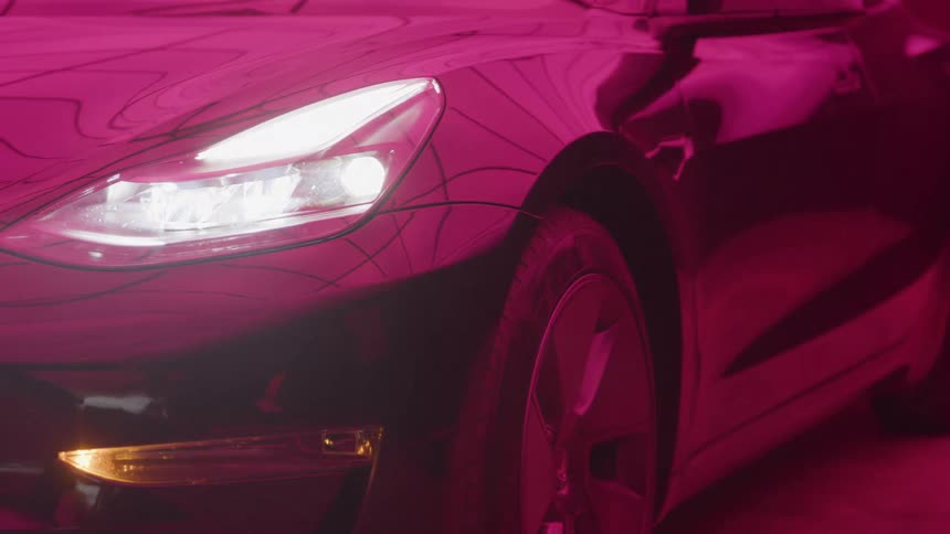 A luxury car driving indoors with pink lights illuminating its bodywork