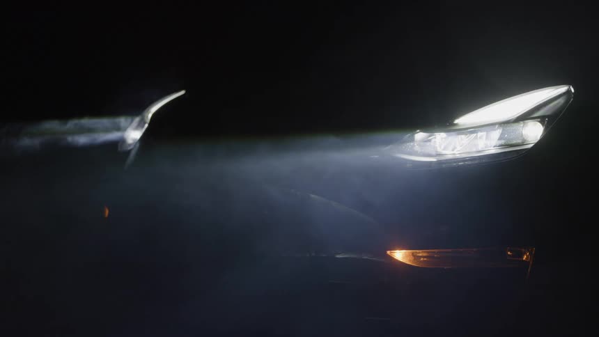 Fog passes by the bright headlights of a parked car at night