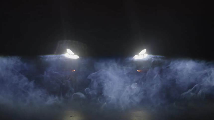 The lights of a car on at night and white smoke passing in front