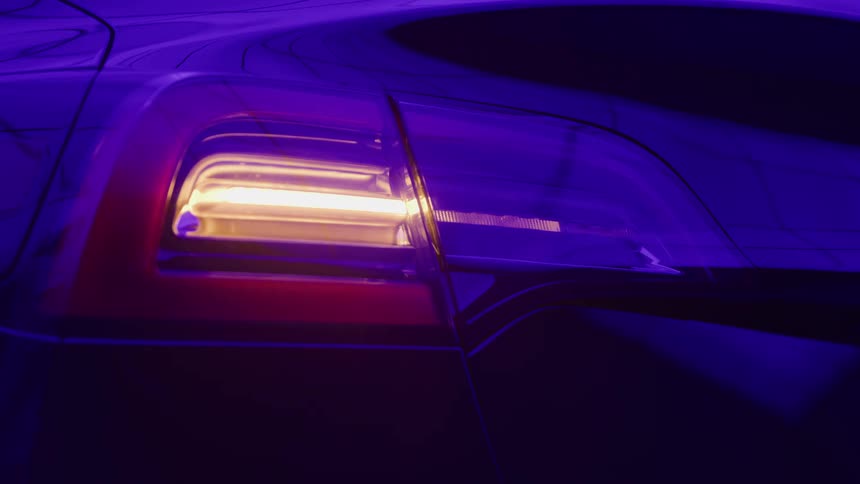 The amber turn signal of a modern car flashes brightly against the dark purple reflections of the vehicle body