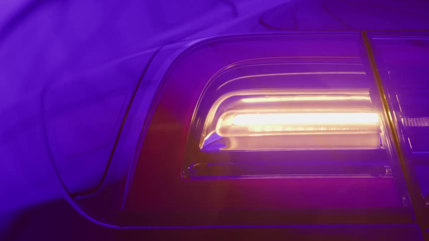 The video is a stylized closeup shot of a cars taillight under a bright yelloworange lightthe entire scene is bathed in an intense purple ambient color creating a highcontrast and saturated futuristic look